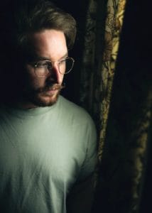 man wearing eyeglasses looking outside curtains